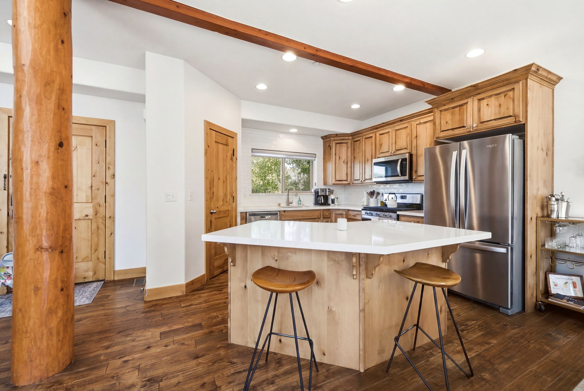 Spacious kitchen featuring a central island with white countertop, rich wood-finish flooring, custom wood cabinetry, stainless steel appliances, and recessed lighting