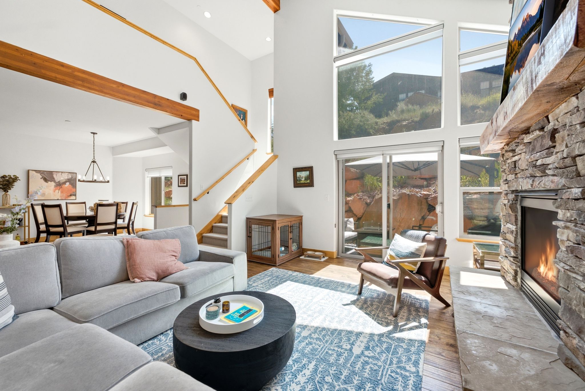 Spacious living area featuring a stone-clad fireplace with a natural wood mantel, a multi-pane window wall, and a sliding glass door