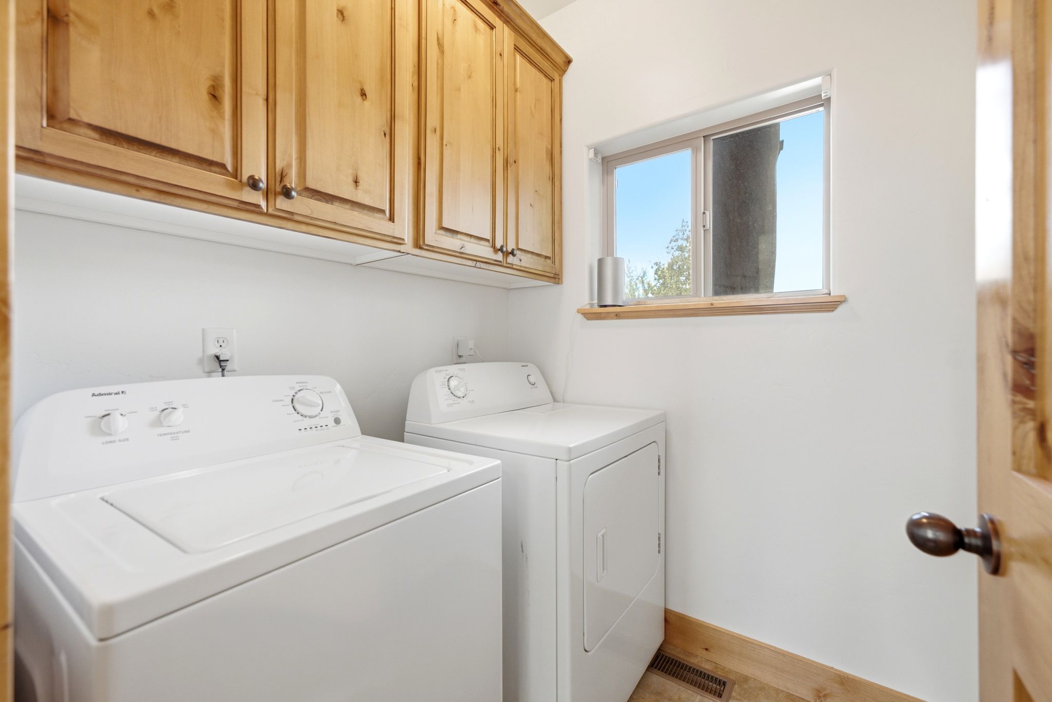 Laundry area featuring light wood-finish cabinetry, a window with wood trim, and wood-finish baseboards