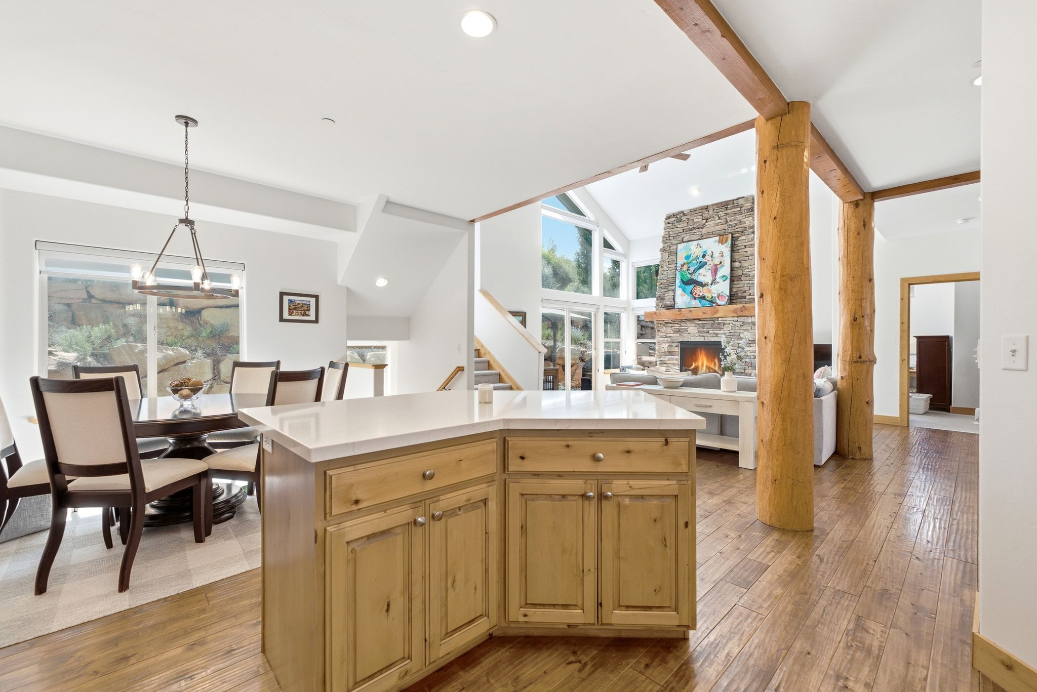 Open-concept living area featuring wood-finish flooring, a stone fireplace, and exposed wood beams