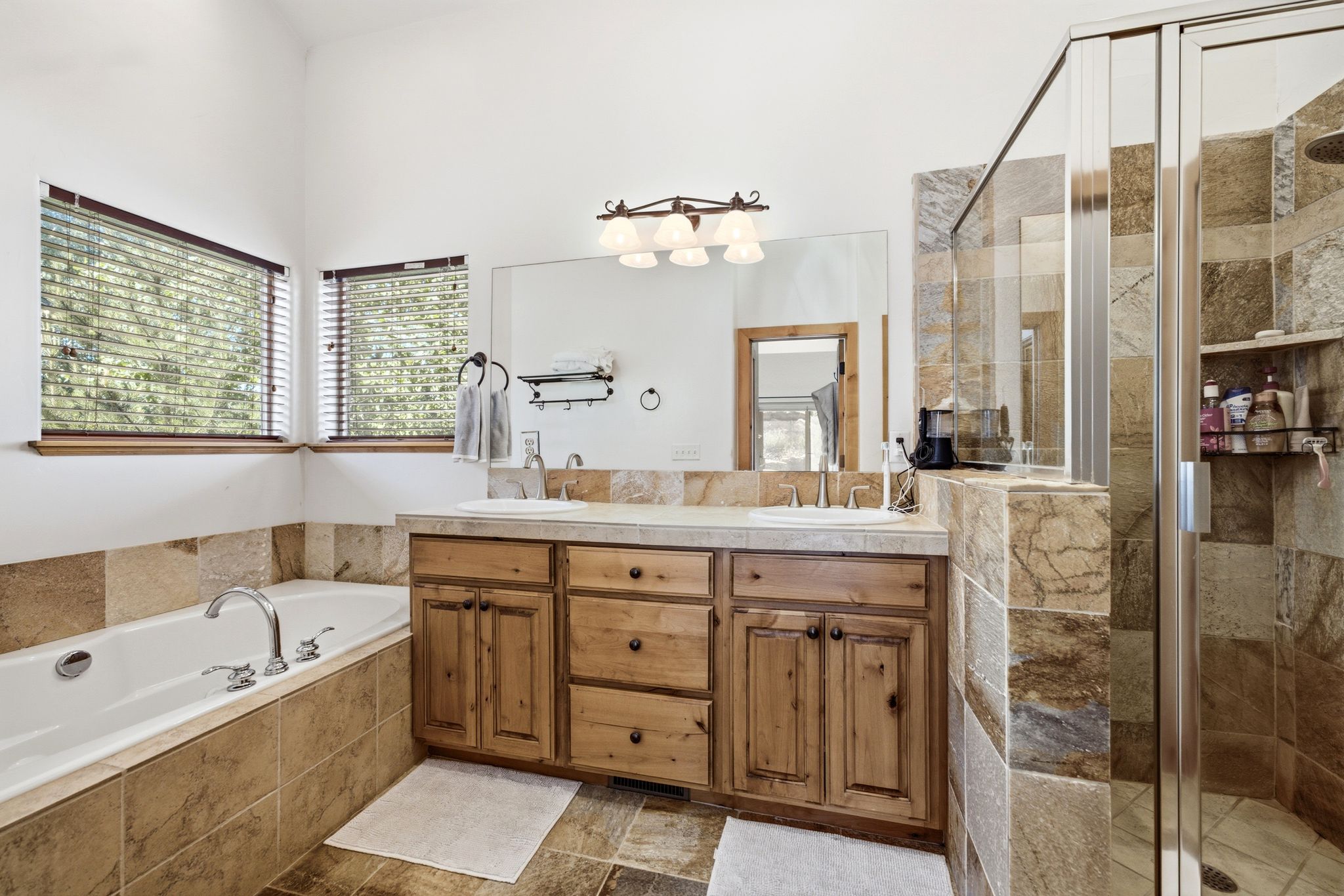Bathroom featuring a full-size bathtub, dual vanity with wood cabinetry, tile flooring, and a walk-in shower with clear glass enclosure