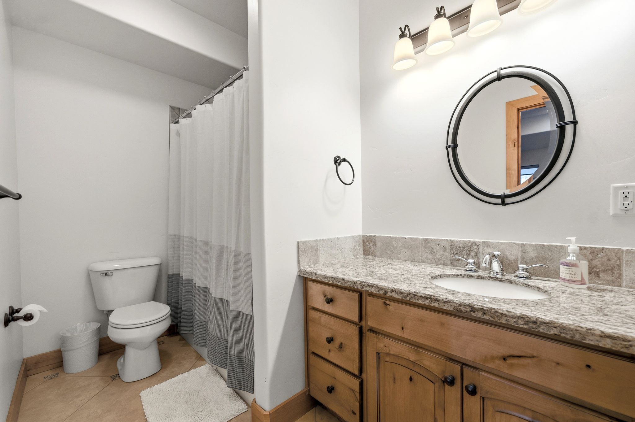 Bathroom featuring a wood-finish vanity with a granite countertop, undermount sink, and a circular framed mirror