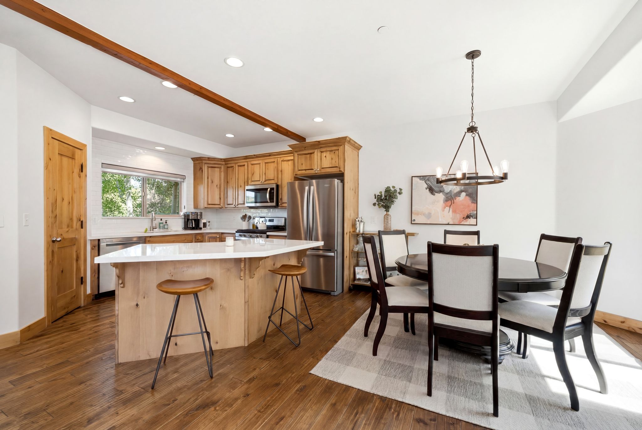 Open-concept kitchen and dining area featuring warm wood-finish flooring, a kitchen island with a light-toned countertop, stainless steel appliances, and a dining space illuminated by a circular chandelier