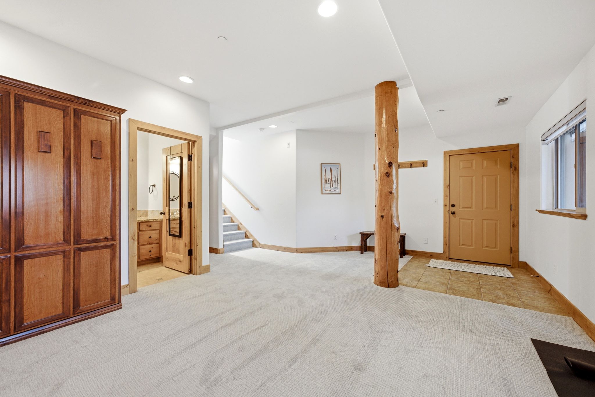Spacious carpeted area featuring a natural wood support column, light wood paneled entry door, and built-in cabinetry