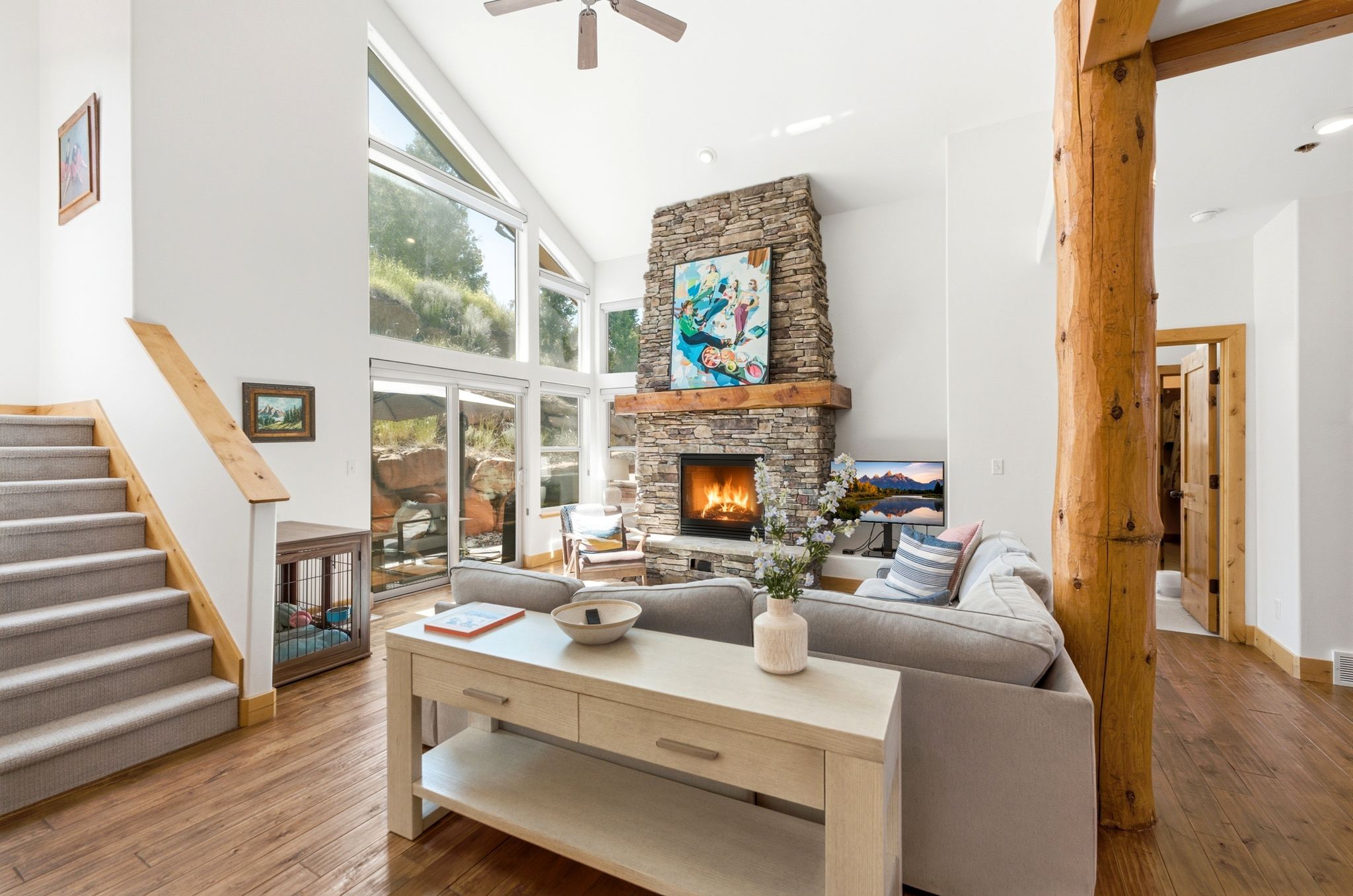 Spacious living area featuring a stone fireplace, vaulted ceilings, and large windows