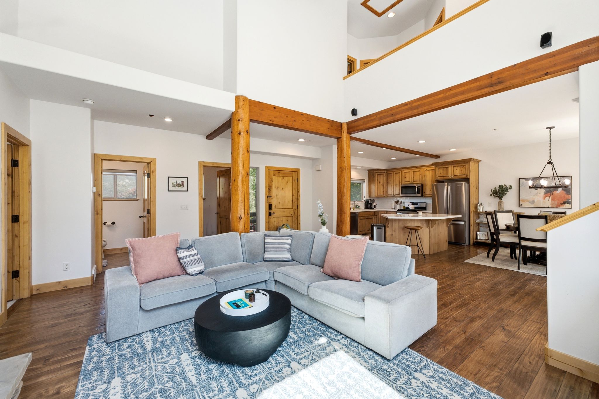 Open-concept living space featuring wood-finish flooring, exposed wood beams, and a two-story ceiling