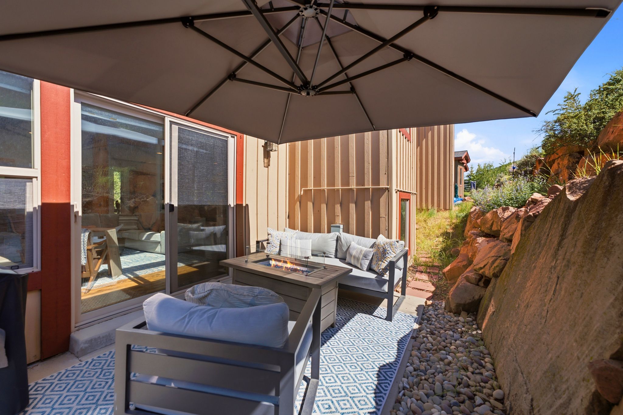 Outdoor patio featuring a large umbrella, concrete flooring with a geometric rug, and a built-in fire pit