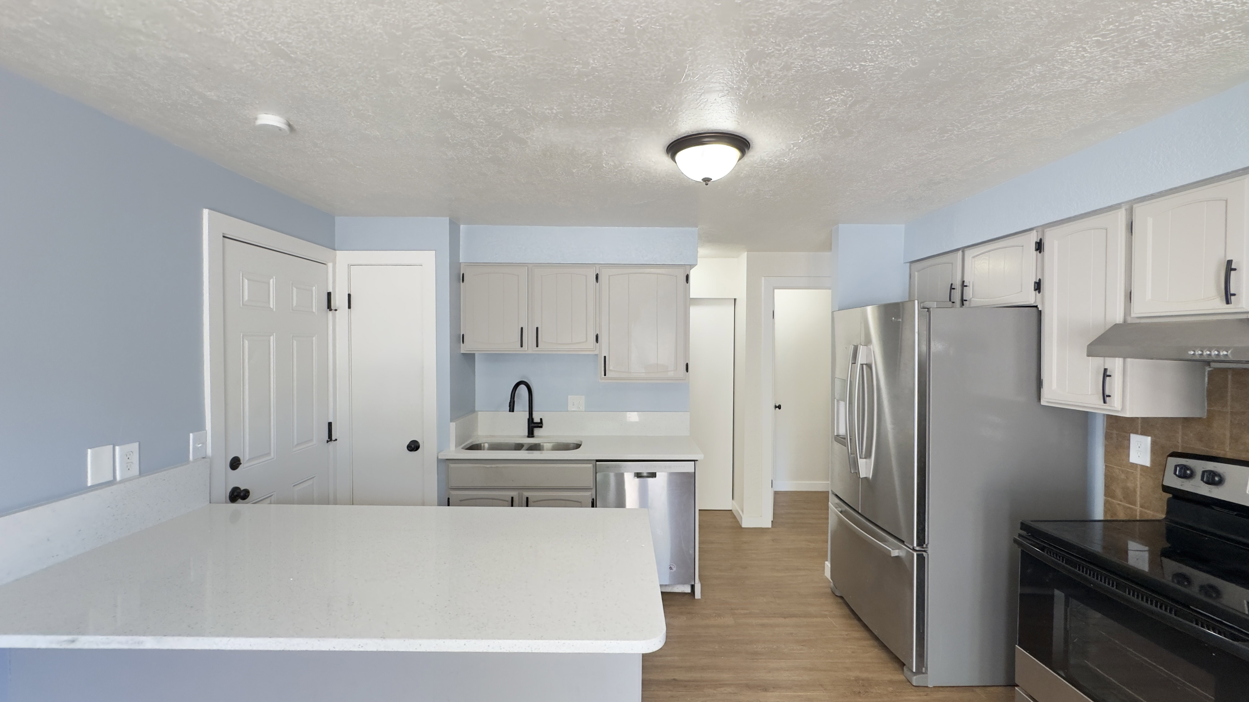 Kitchen featuring white shaker-style cabinetry, stainless steel appliances, a premium white corian countertops, and wood-finish flooring.