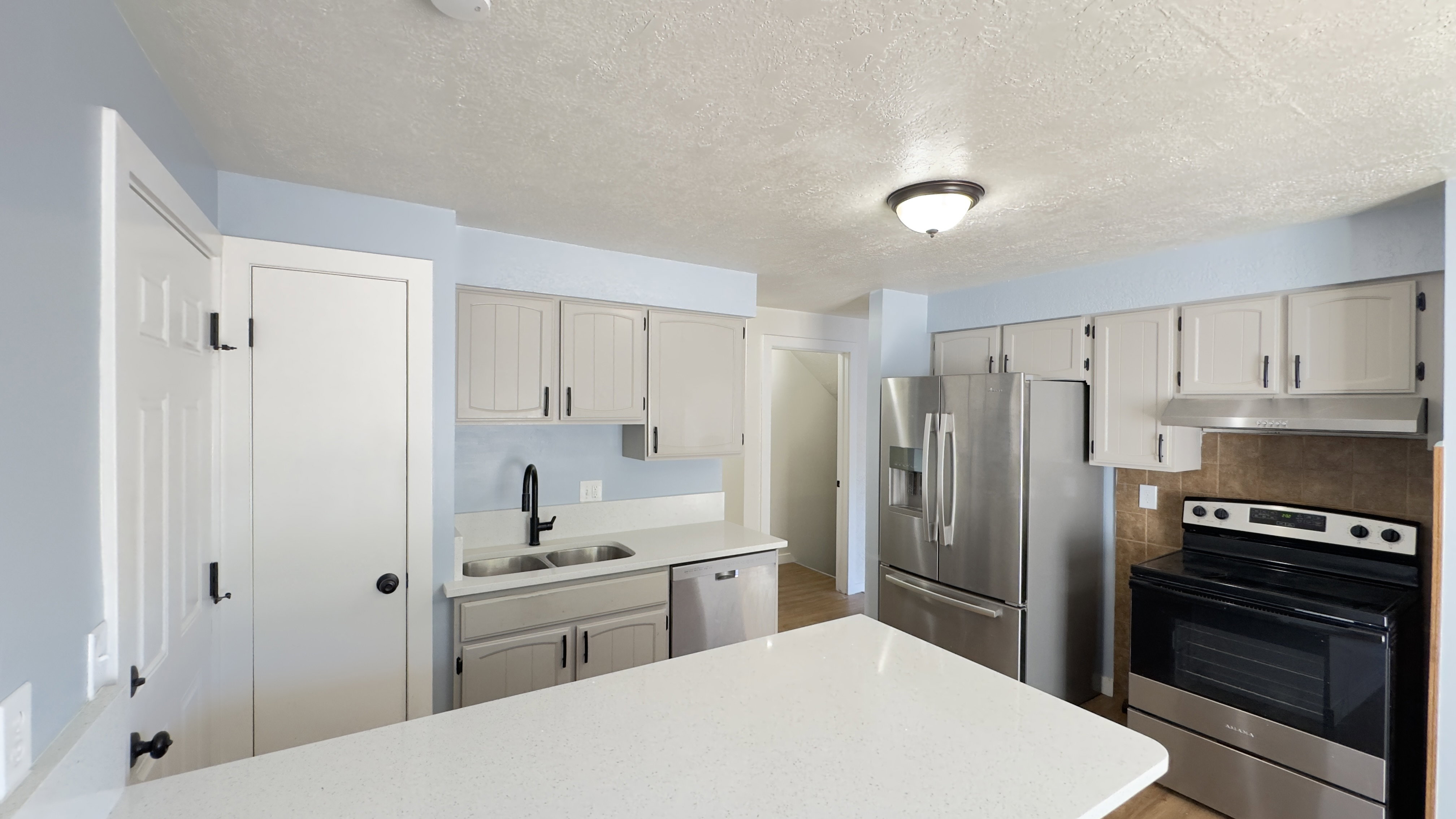 Kitchen featuring white cabinetry, stainless steel appliances, a white countertop island, and a dual-basin sink with a matte black faucet