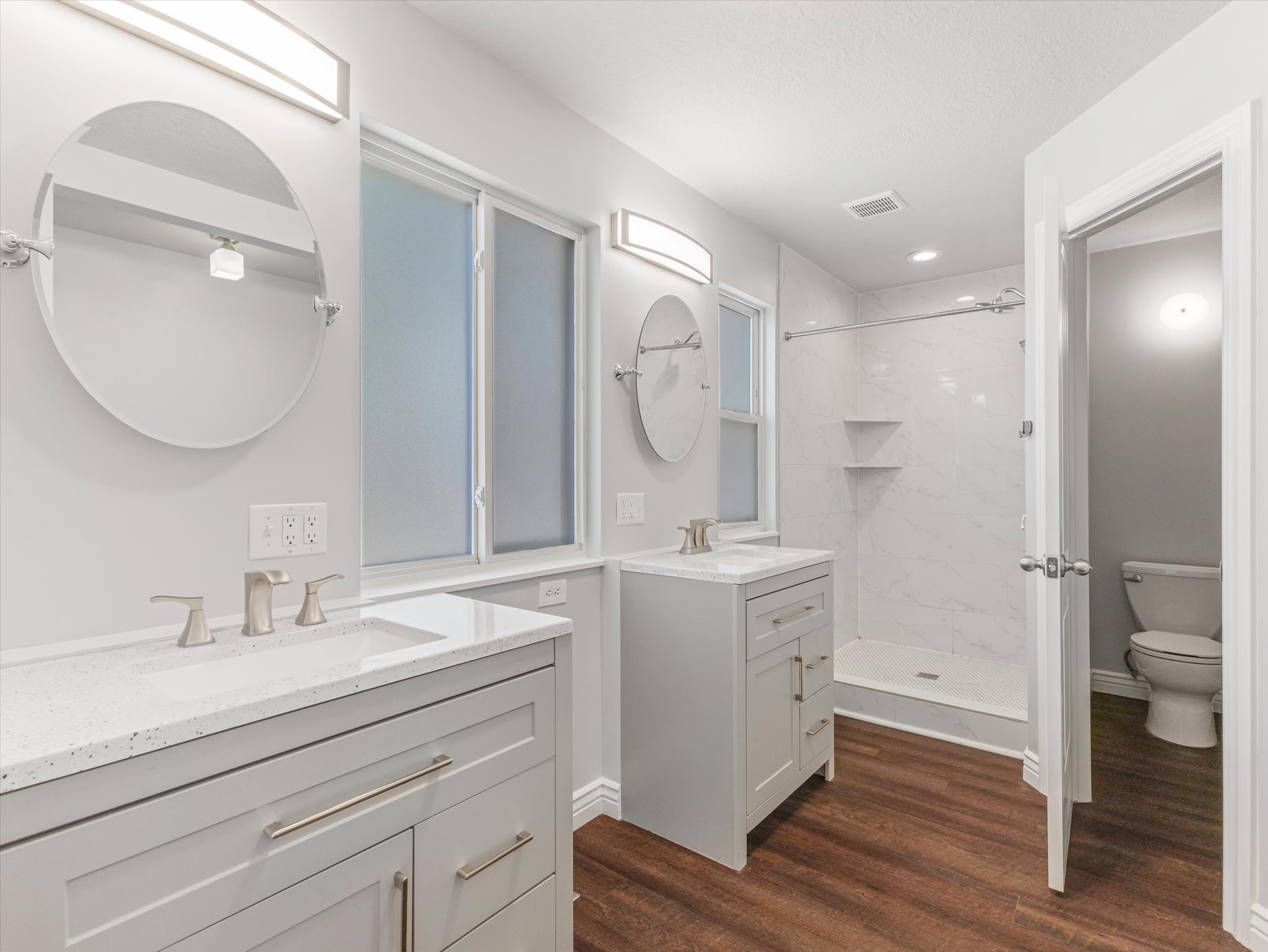 Bathroom featuring dual vanity sinks with light gray cabinetry, white countertops, and brushed nickel fixtures