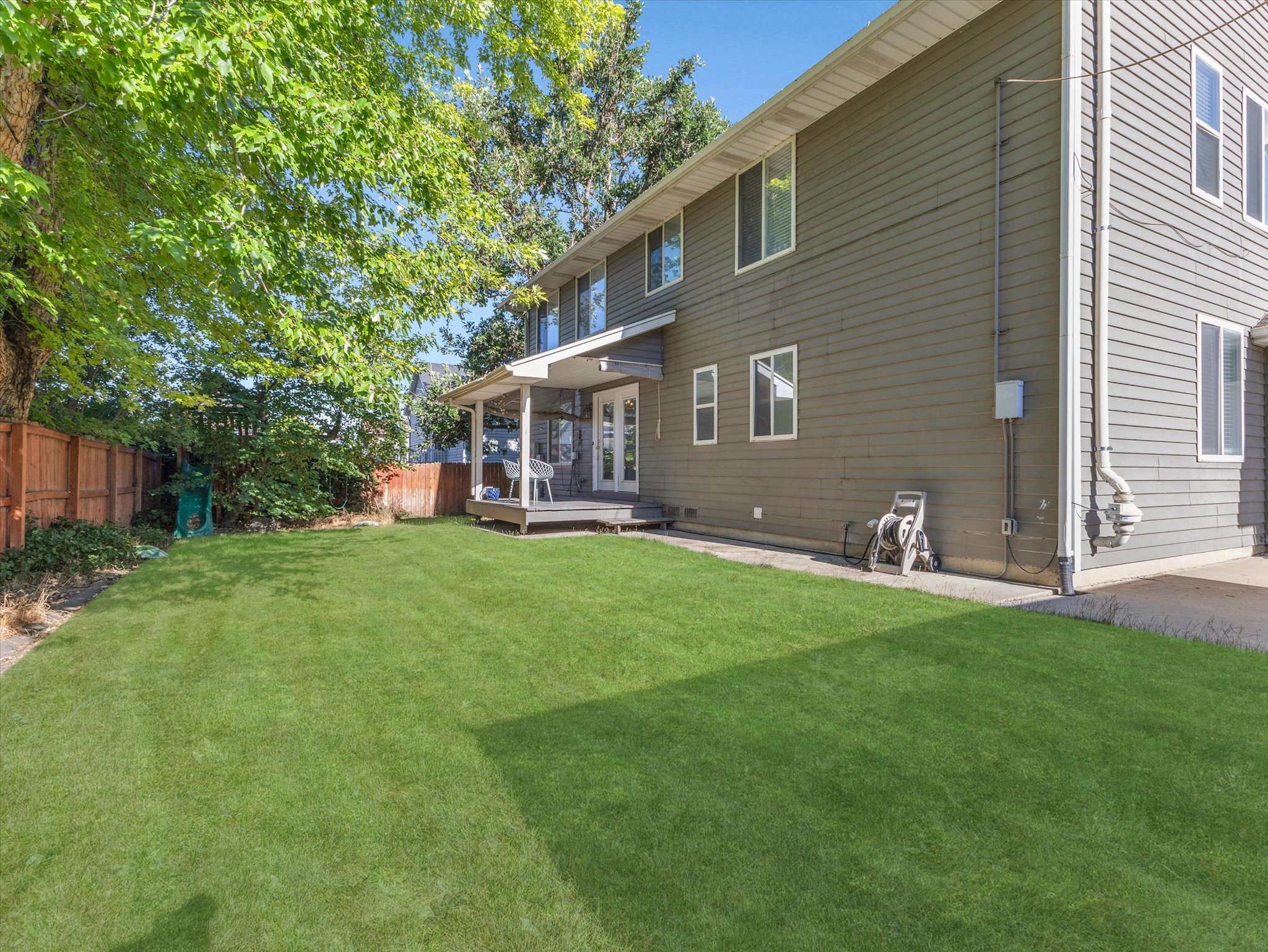 Spacious backyard featuring a manicured lawn, wood fencing, and mature trees providing natural shade