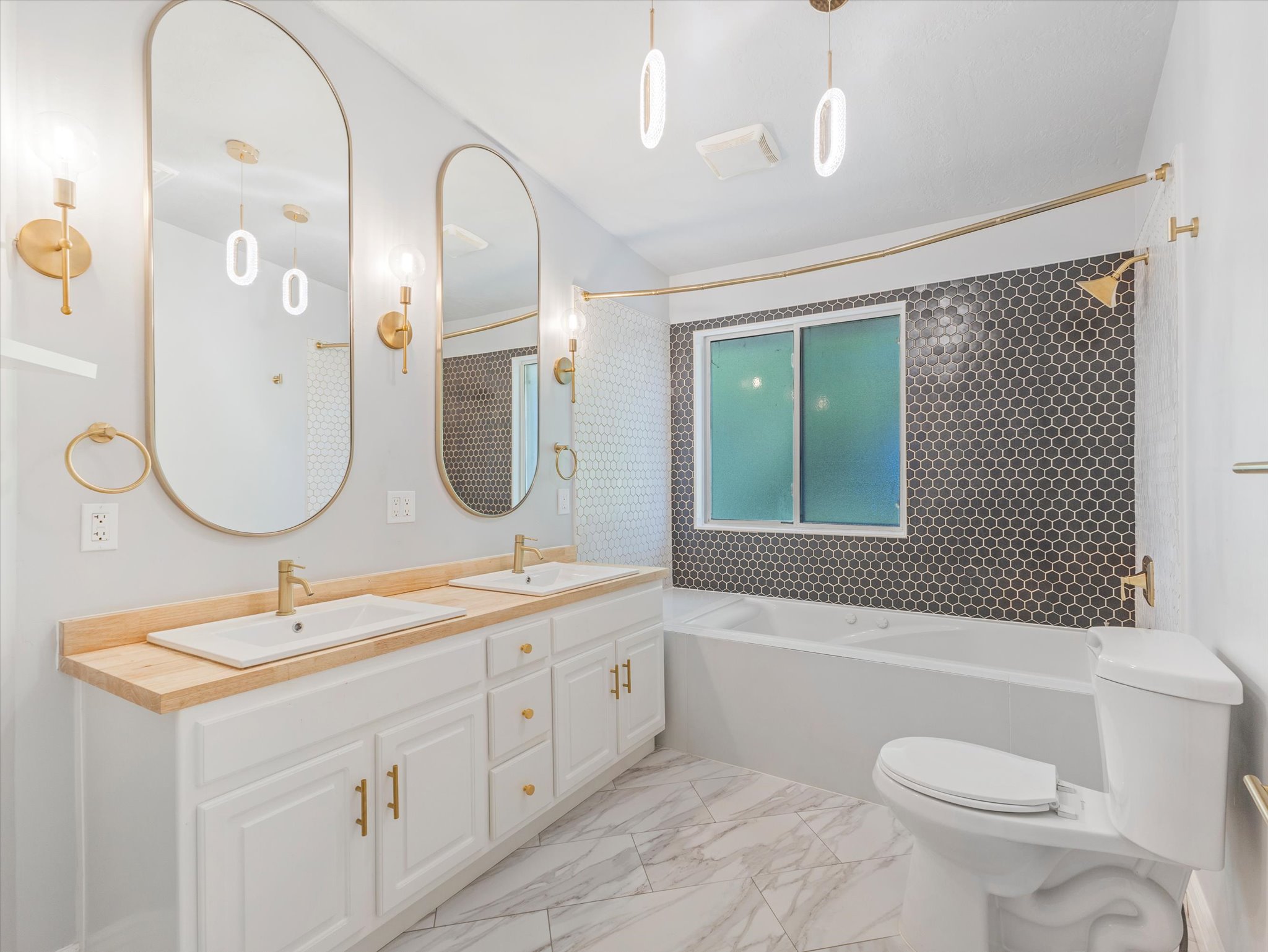 Bathroom featuring a double vanity with wood-finish countertop, white cabinetry, and gold-tone hardware