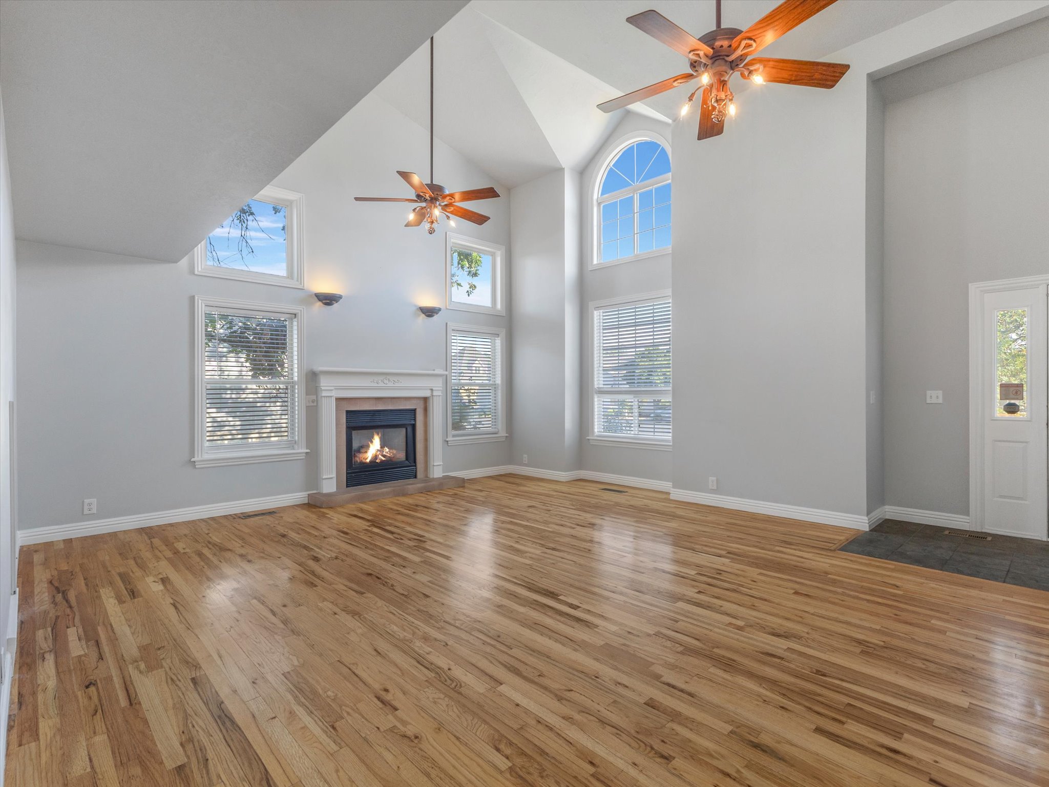 Spacious living area featuring vaulted ceilings, wood-finish flooring, and a fireplace with a decorative mantel