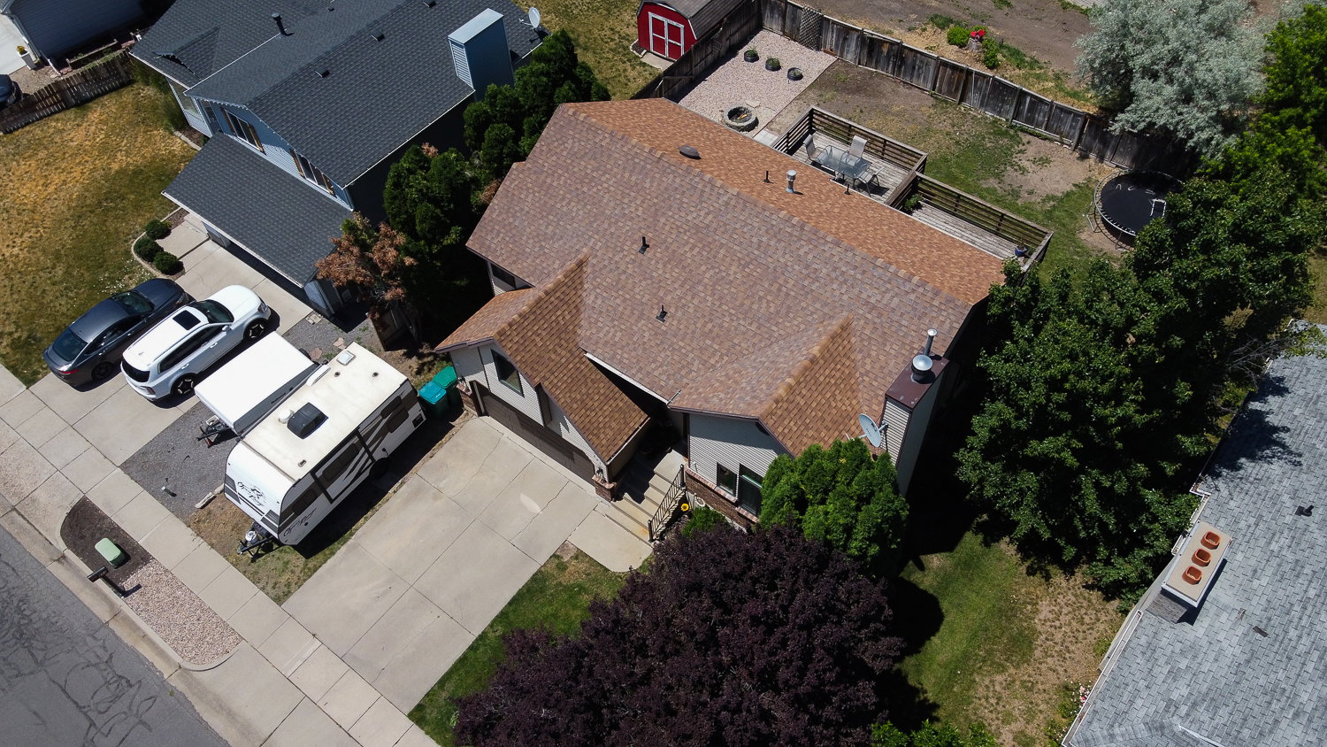 Residential property featuring a brown shingle roof, attached garage, concrete driveway, and mature landscaping