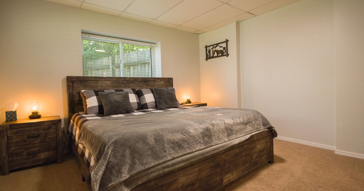 Carpeted bedroom featuring a window with white blinds, light-toned walls, and a drop ceiling