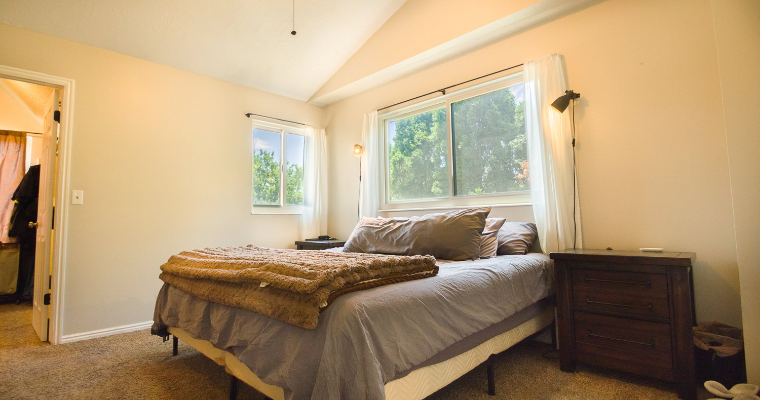 Vaulted ceiling room with carpet flooring and two windows featuring white window treatments