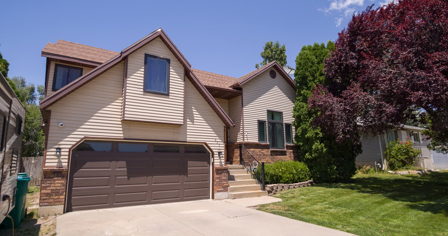 Split-level exterior featuring tan siding, a brown garage door, and a brown shingle roof