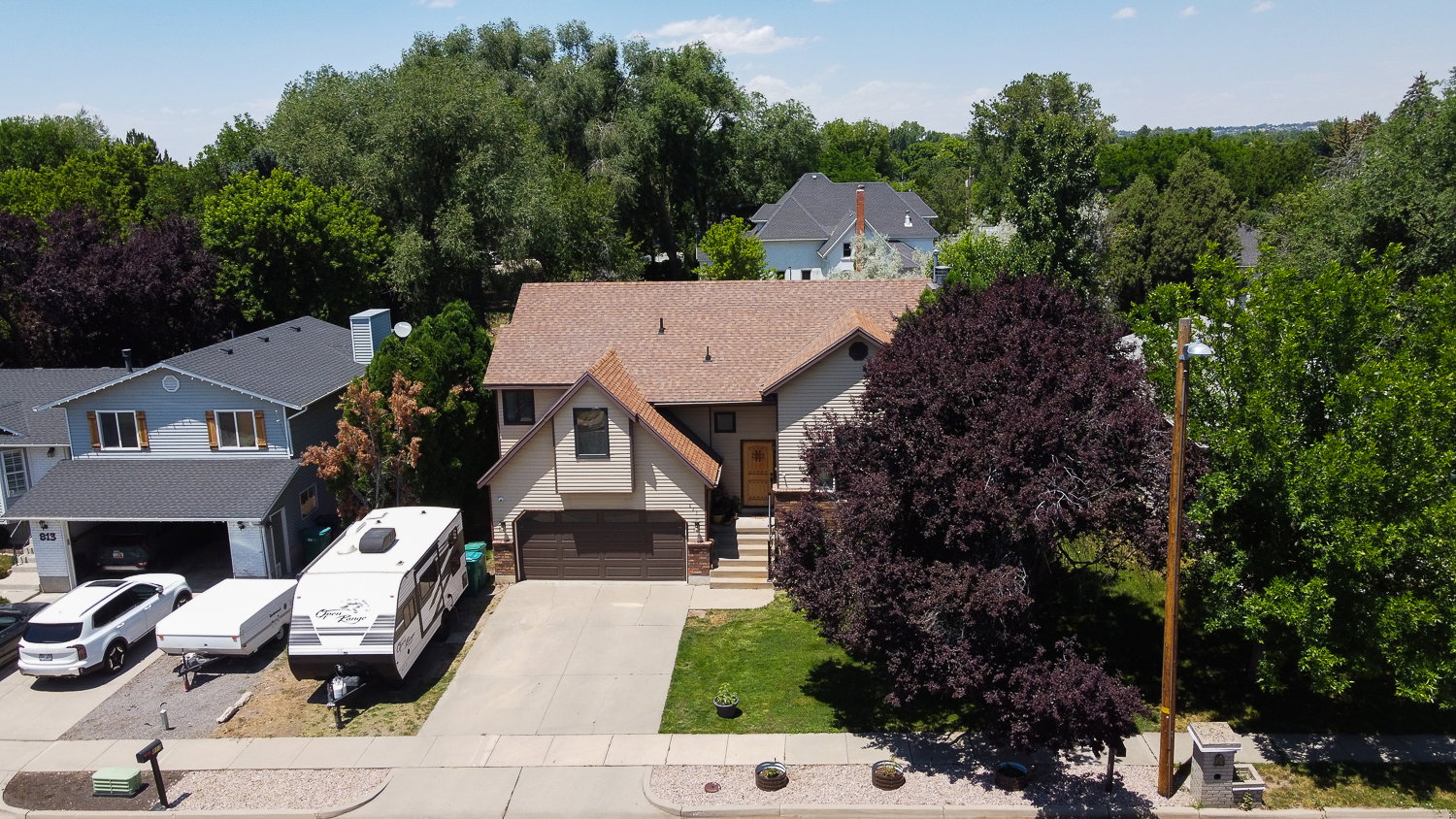 Traditional-style residence featuring a two-car garage, established front yard landscaping with mature trees, and a concrete driveway