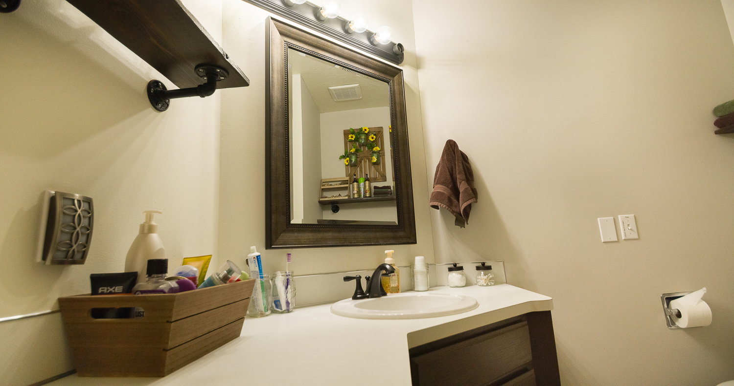 Bathroom vanity with a white countertop and integrated sink, framed mirror, wall-mounted lighting, and a dark wood-finish cabinet