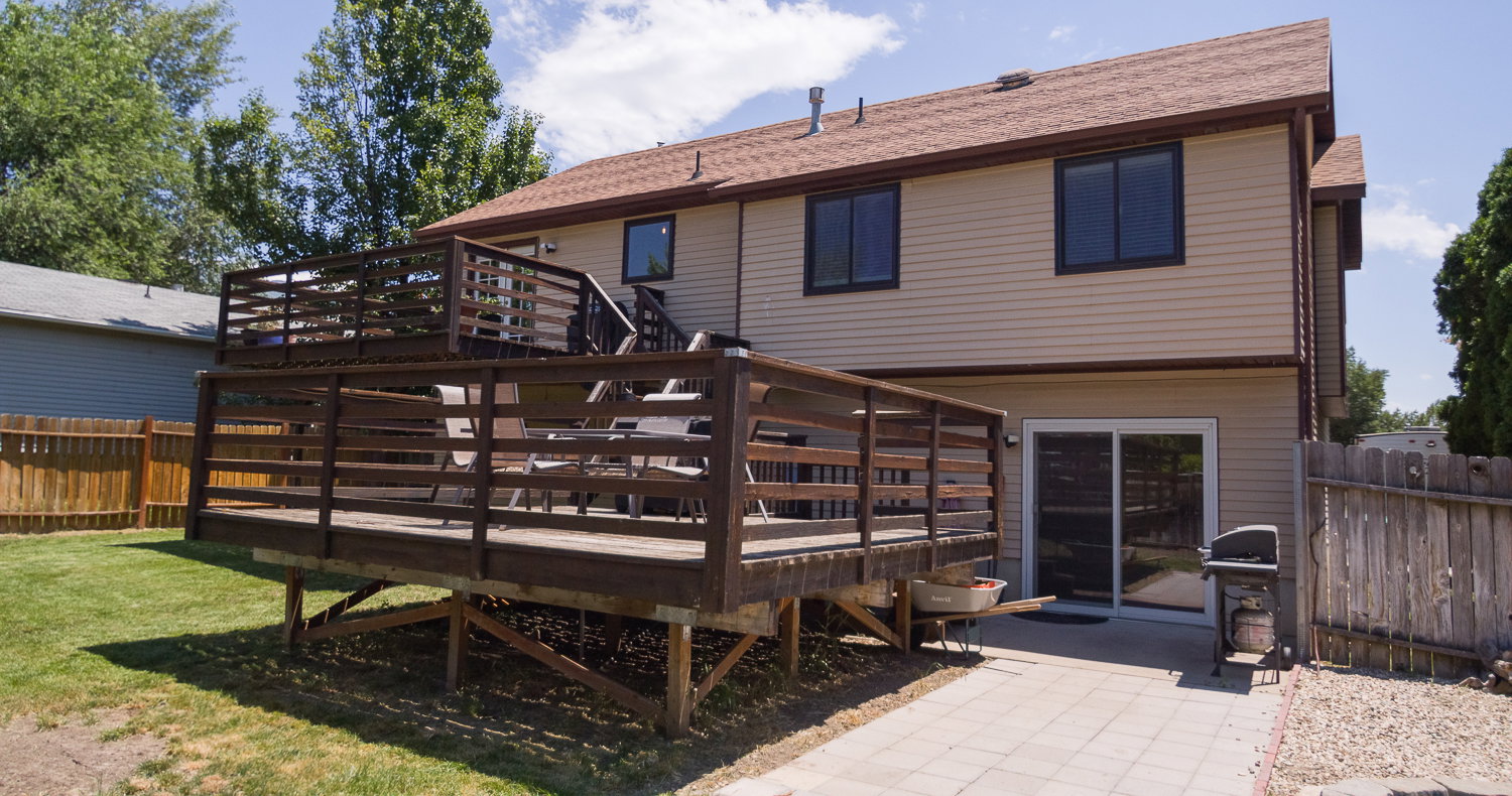 Two-story wood deck with railing, accessible from the upper level, overlooking a green lawn