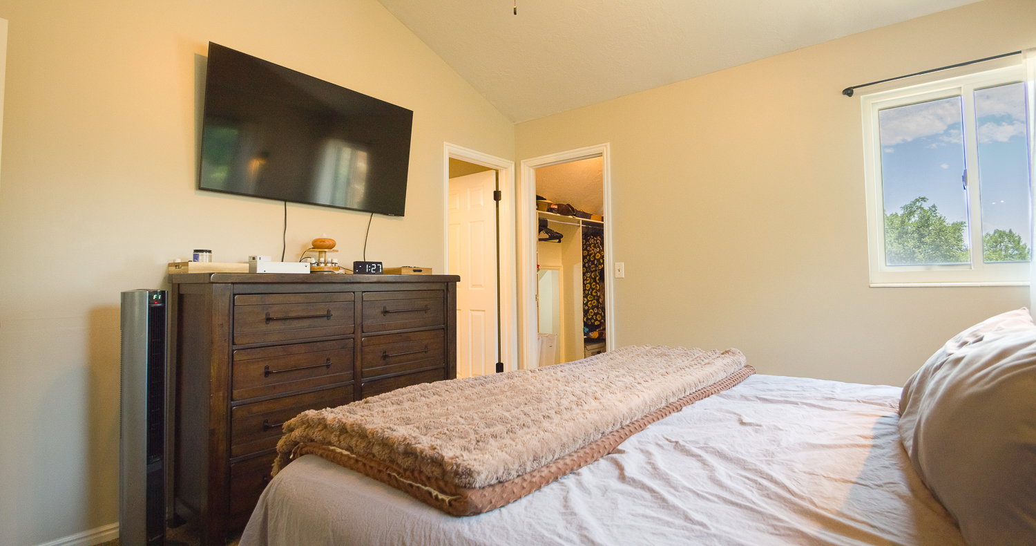 Vaulted ceiling bedroom featuring a double-hung window, soft cream wall paint, and a walk-in closet entryway