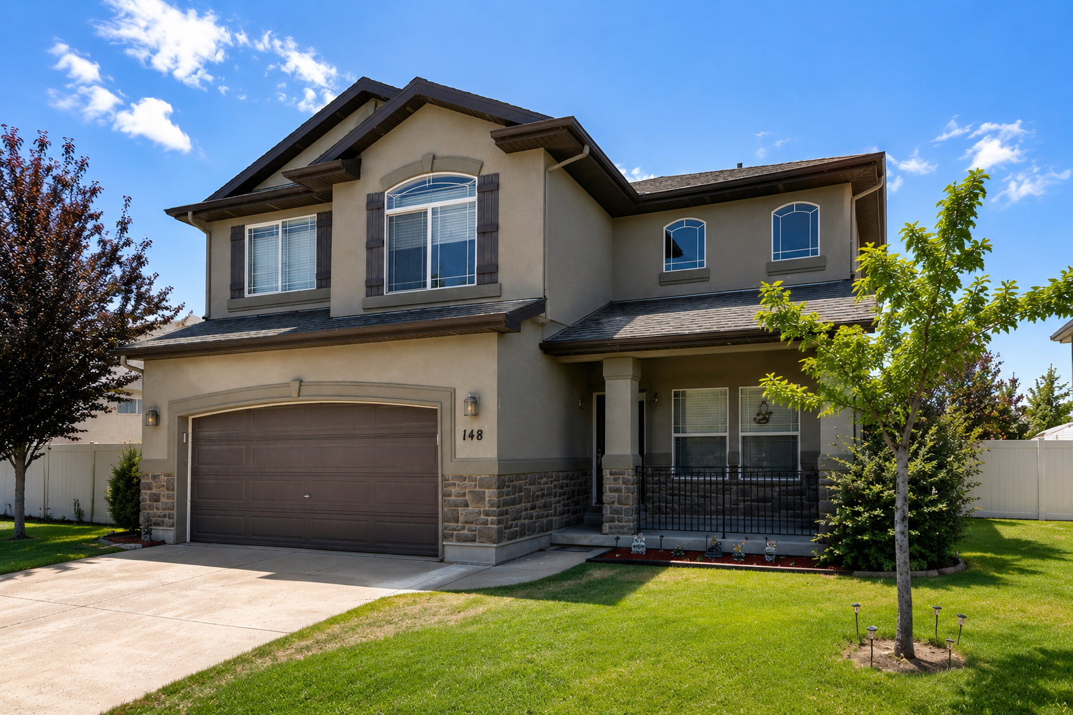 Two-story stucco residence with stone accents, featuring an integrated two-car garage and a covered front porch with iron railings