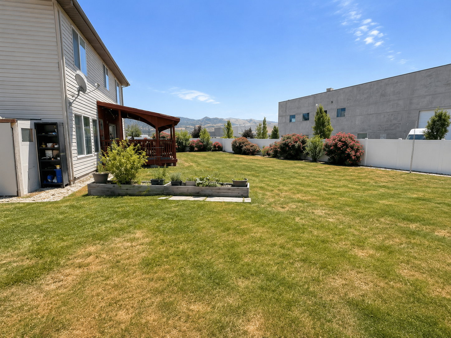Expansive backyard featuring a large lawn, a white privacy fence, and mature landscaping