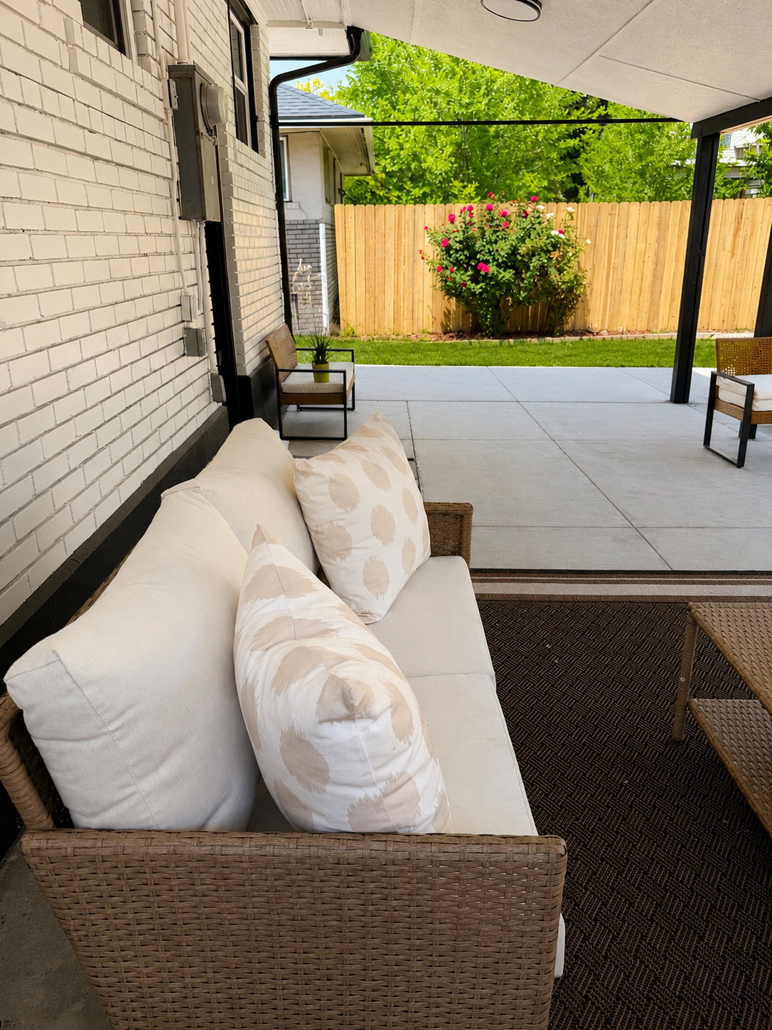 Covered concrete patio featuring a white brick exterior, dark downspout, and a wood fence