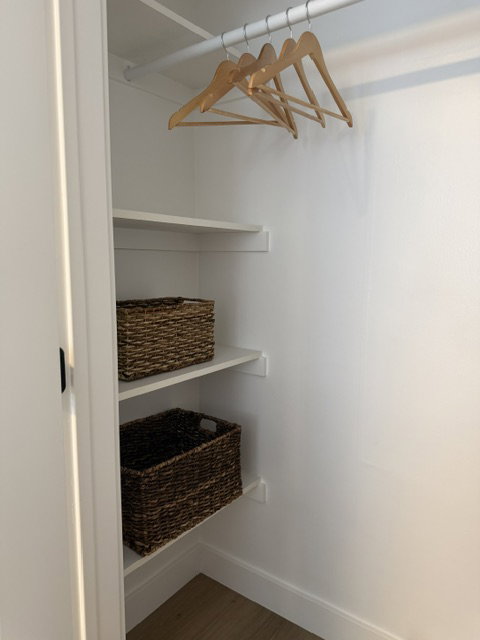 Interior closet featuring a hanging rod, multiple built-in shelves, white painted walls, and wood-finish flooring