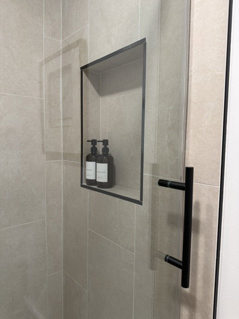 Shower enclosure featuring a built-in niche with black trim, a clear glass panel, a matte black handle, and large format wall tiles