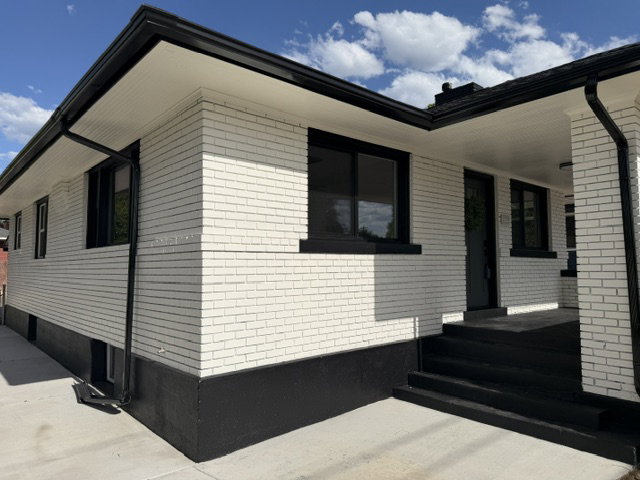 Exterior featuring white brick siding with black trim, black window frames, and a dark entry door