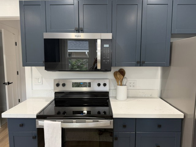 Kitchen featuring dark blue cabinetry, light-toned countertops, stainless steel microwave, and a stainless steel electric range
