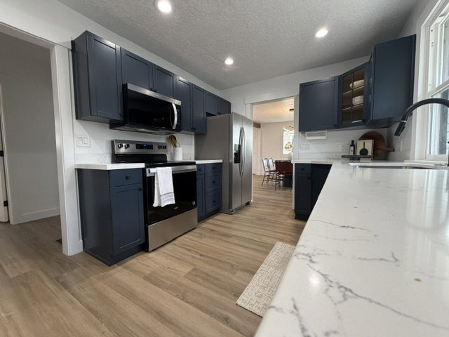 Kitchen featuring dark blue cabinetry, wood-finish flooring, white countertops, stainless steel appliances, and recessed lighting