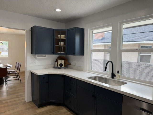 Modern kitchen featuring deep blue cabinetry, light-toned countertops, and a stainless steel sink with a matte black gooseneck faucet