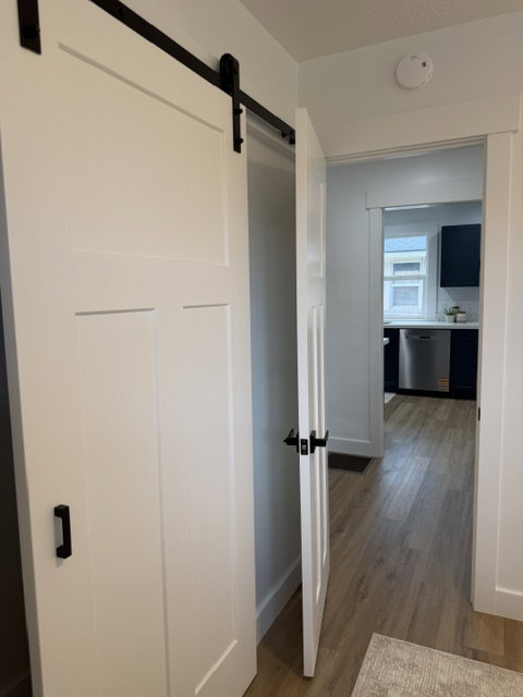 White paneled barn door with black hardware, complementing the light wood-finish flooring