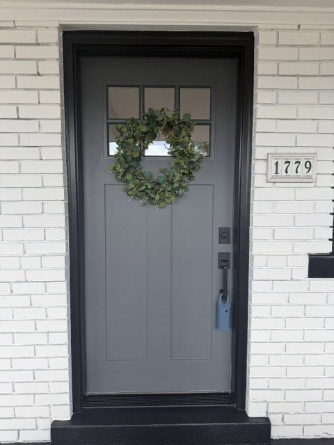 Gray panel door with upper lites, black trim, and white brick exterior