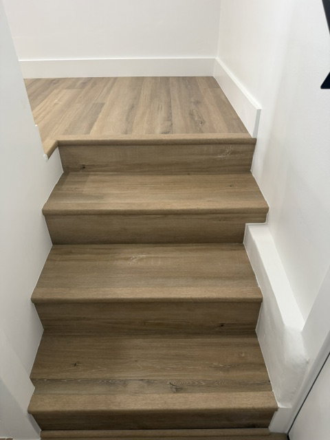 Wood-finish flooring extending from the landing to the staircase with crisp white baseboards