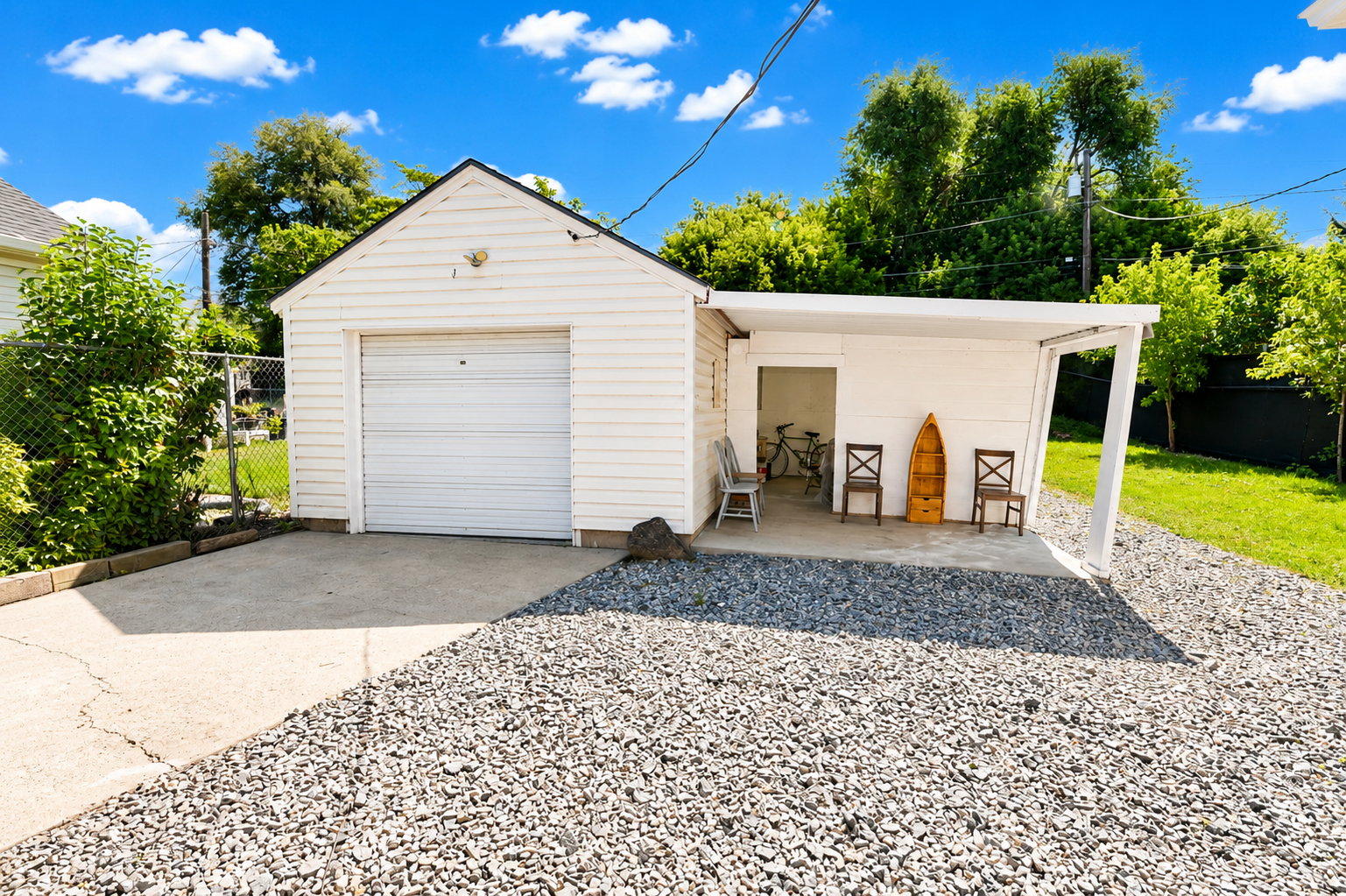 Detached garage with white siding and an overhead door, complemented by an attached covered patio structure