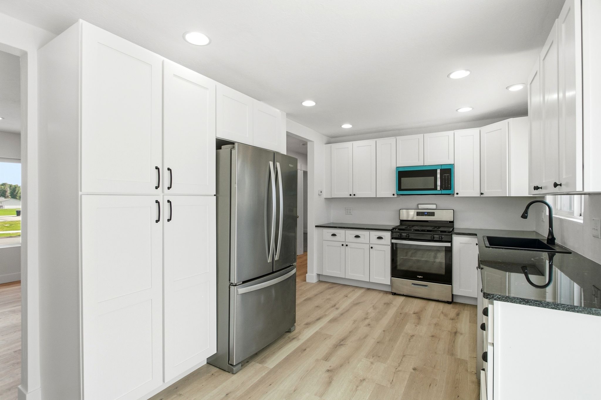 Modern kitchen featuring white shaker cabinetry, stainless steel appliances, dark countertops, and light wood-finish flooring