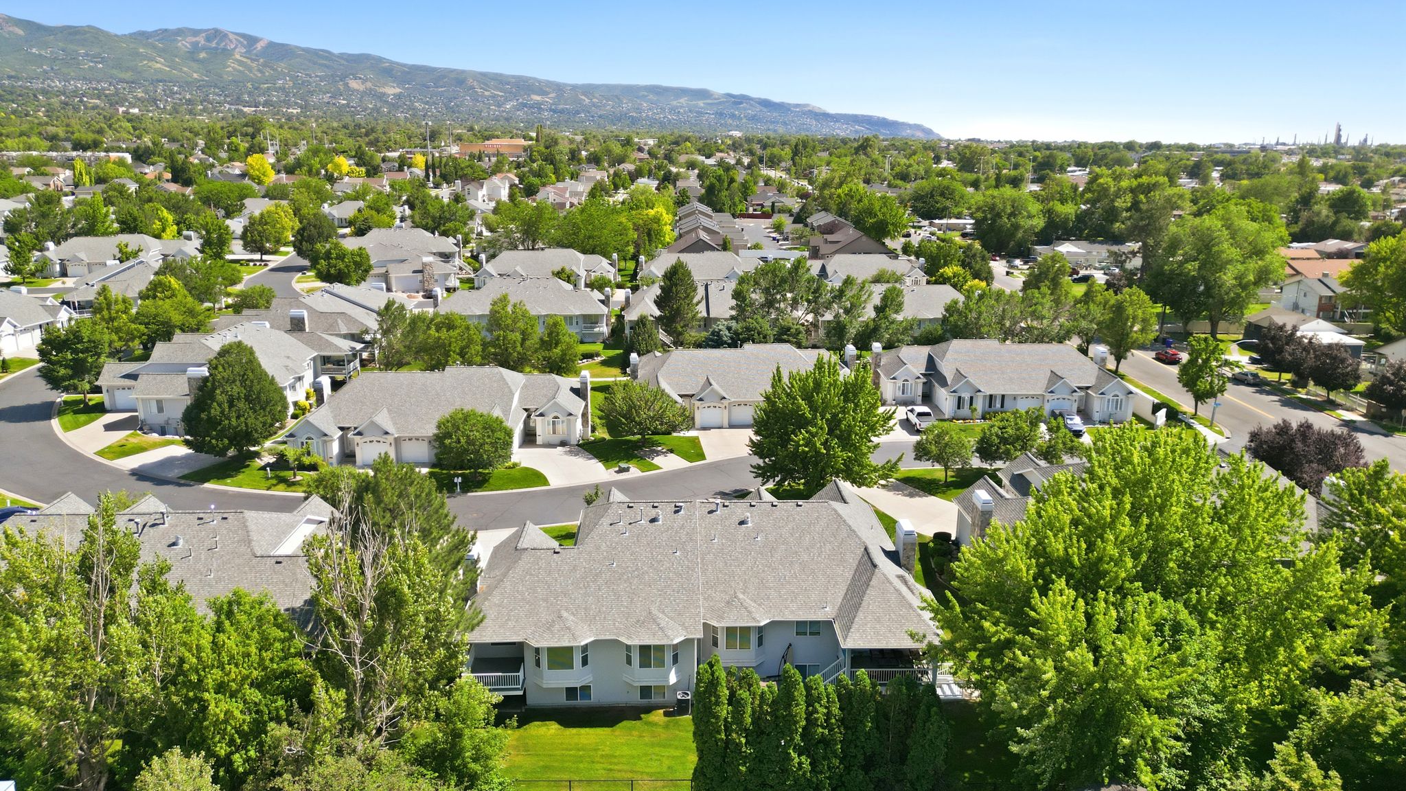 Aerial perspective of a residential neighborhood featuring established homes with gray shingle roofs, mature trees, and paved streets