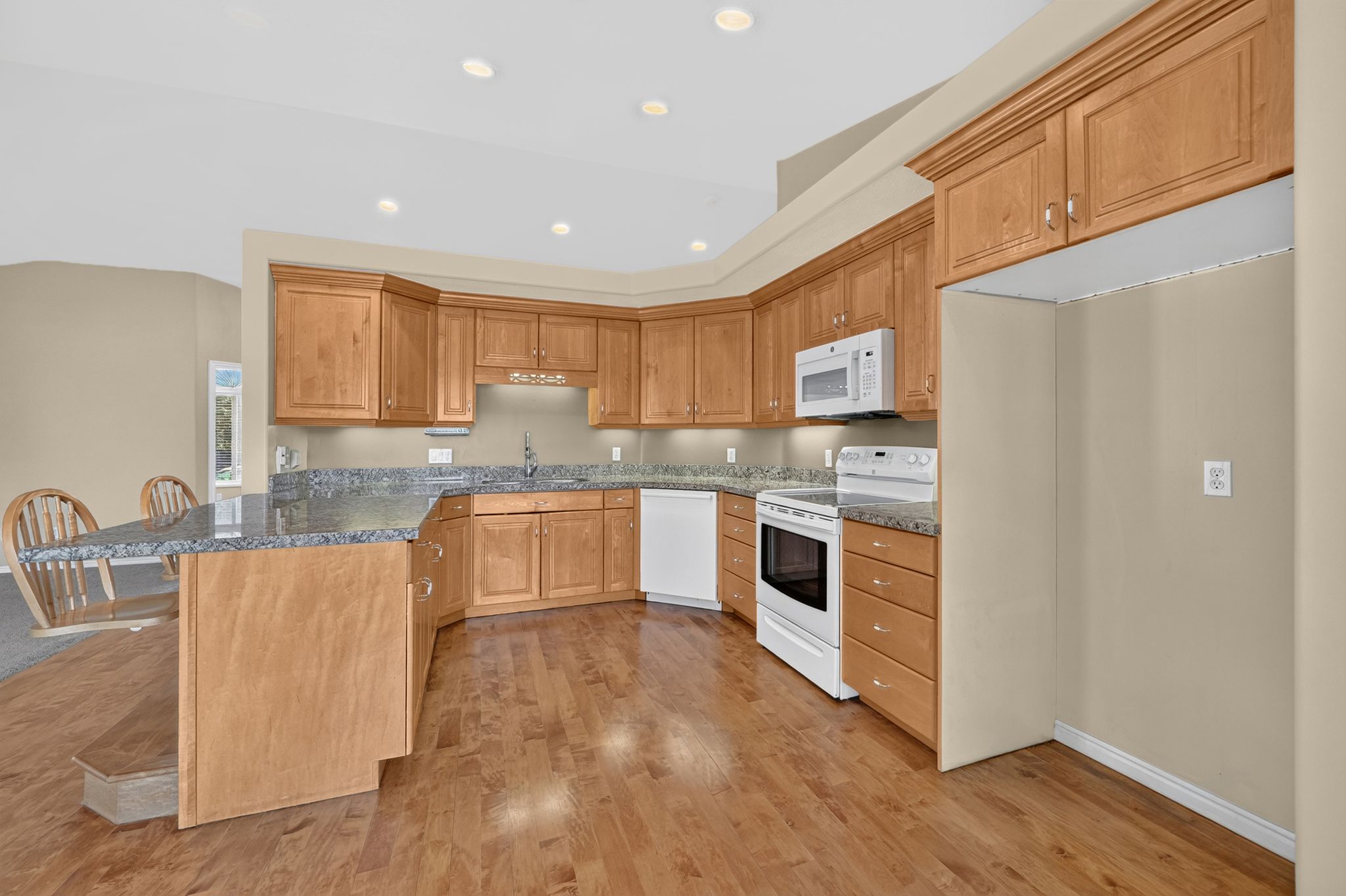 Kitchen featuring wood-finish flooring, a wraparound breakfast bar, wood cabinetry, granite countertops, and recessed lighting