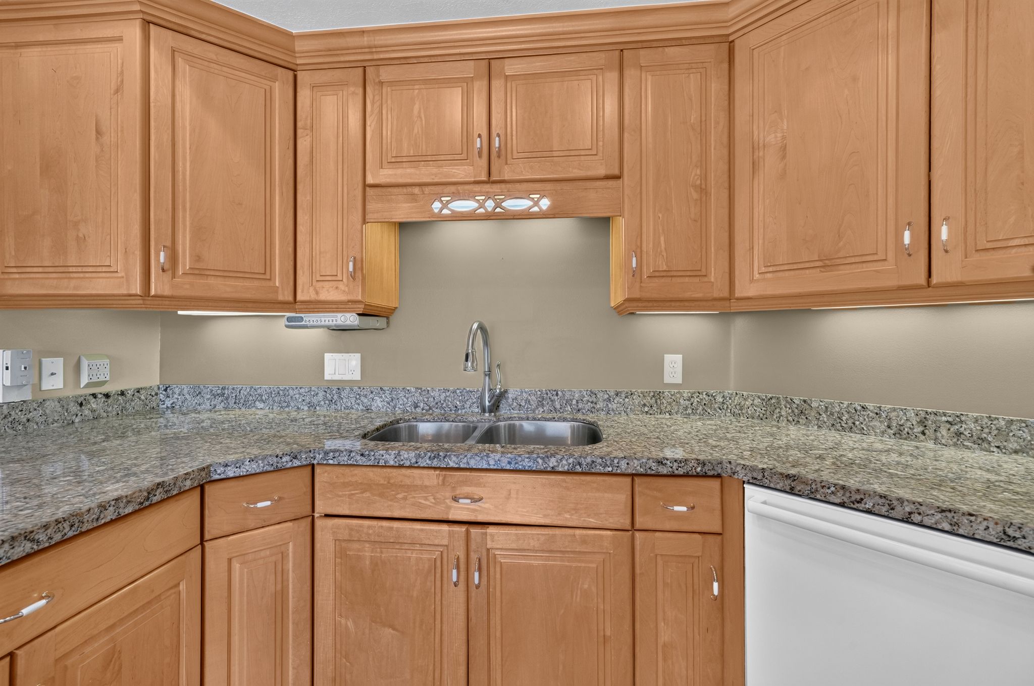 Kitchen featuring light wood cabinetry with crown molding, stone countertops, a double basin sink with a gooseneck faucet, and under-cabinet lighting