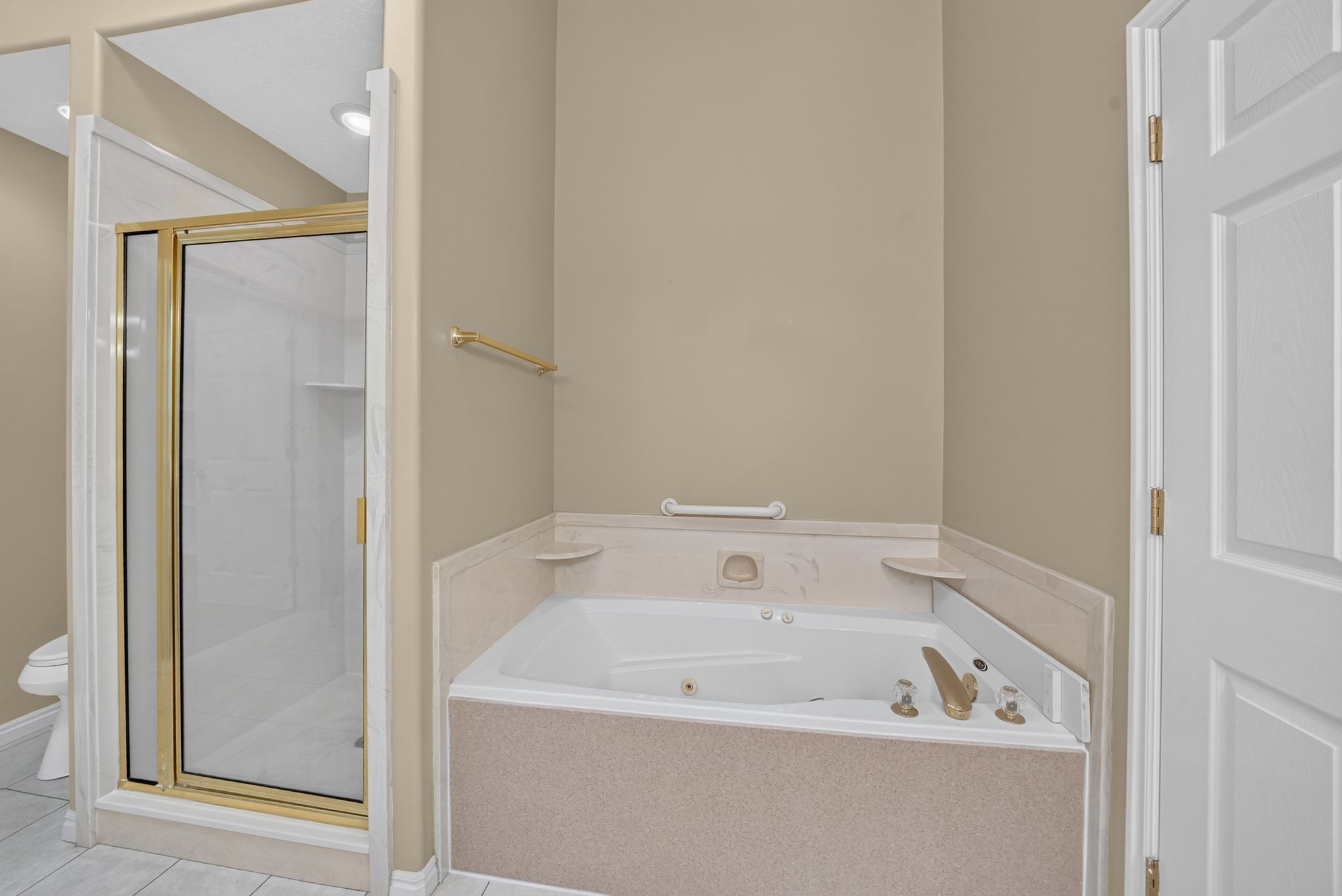 Bathroom featuring a built-in jetted tub with gold-toned fixtures, a framed glass shower enclosure, beige wall paint, a white paneled door, and recessed lighting