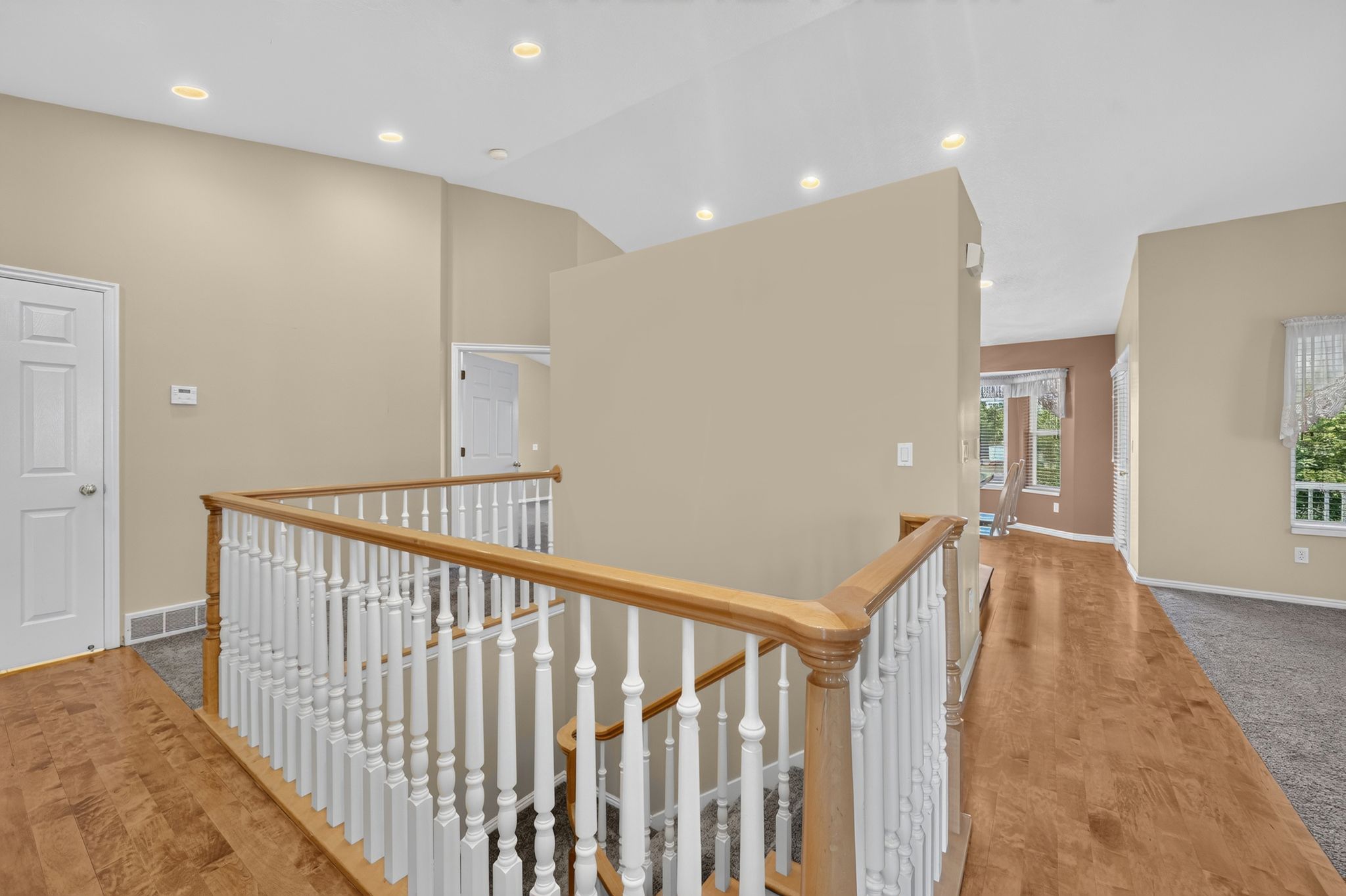 Upper-level landing featuring a wood handrail with white balusters, recessed lighting, and a combination of wood-finish flooring and carpeting