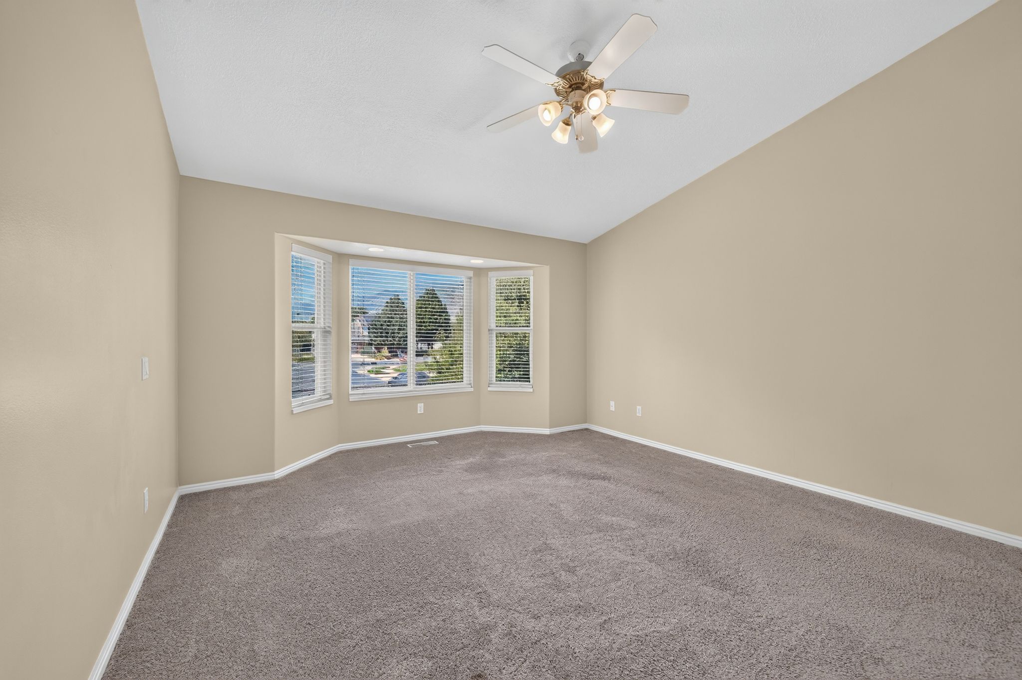 Spacious room featuring a bay window with blinds, vaulted ceiling, and a ceiling fan with integrated lighting
