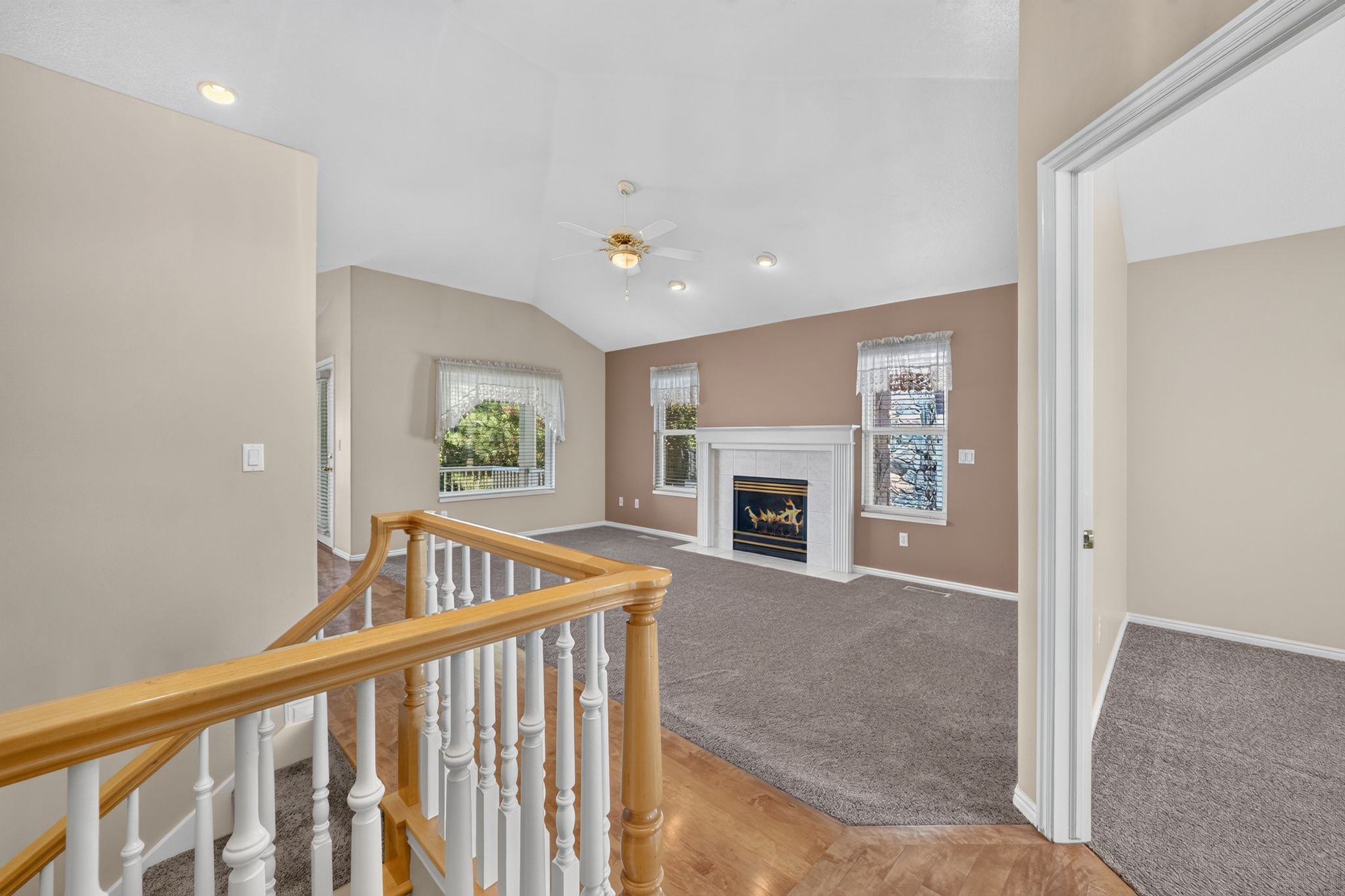 Living area featuring a vaulted ceiling with recessed lighting and a ceiling fan, a white mantel fireplace, and multiple windows