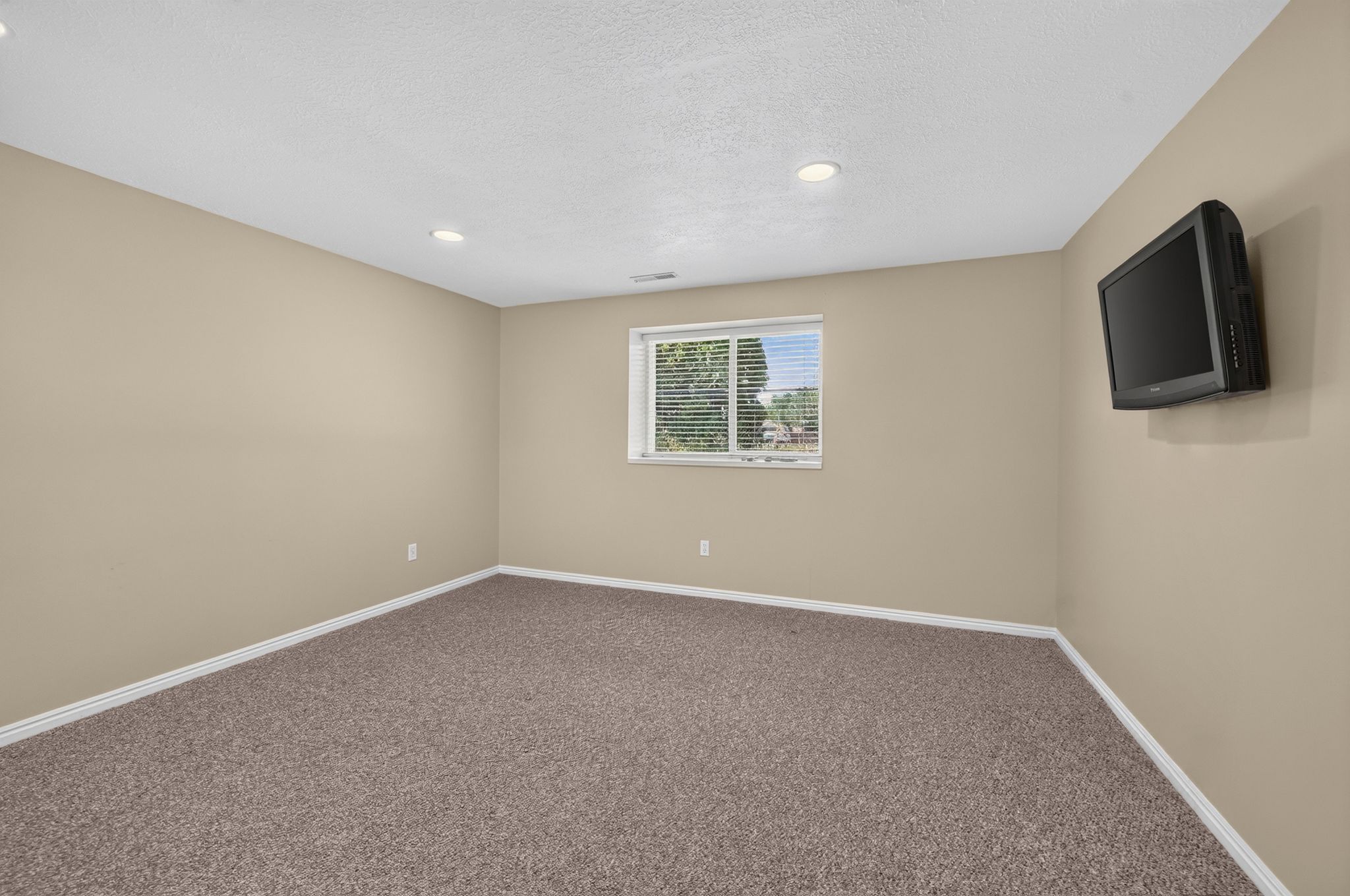 Neutral-toned room featuring recessed lighting, a window with horizontal blinds, and textured carpeting