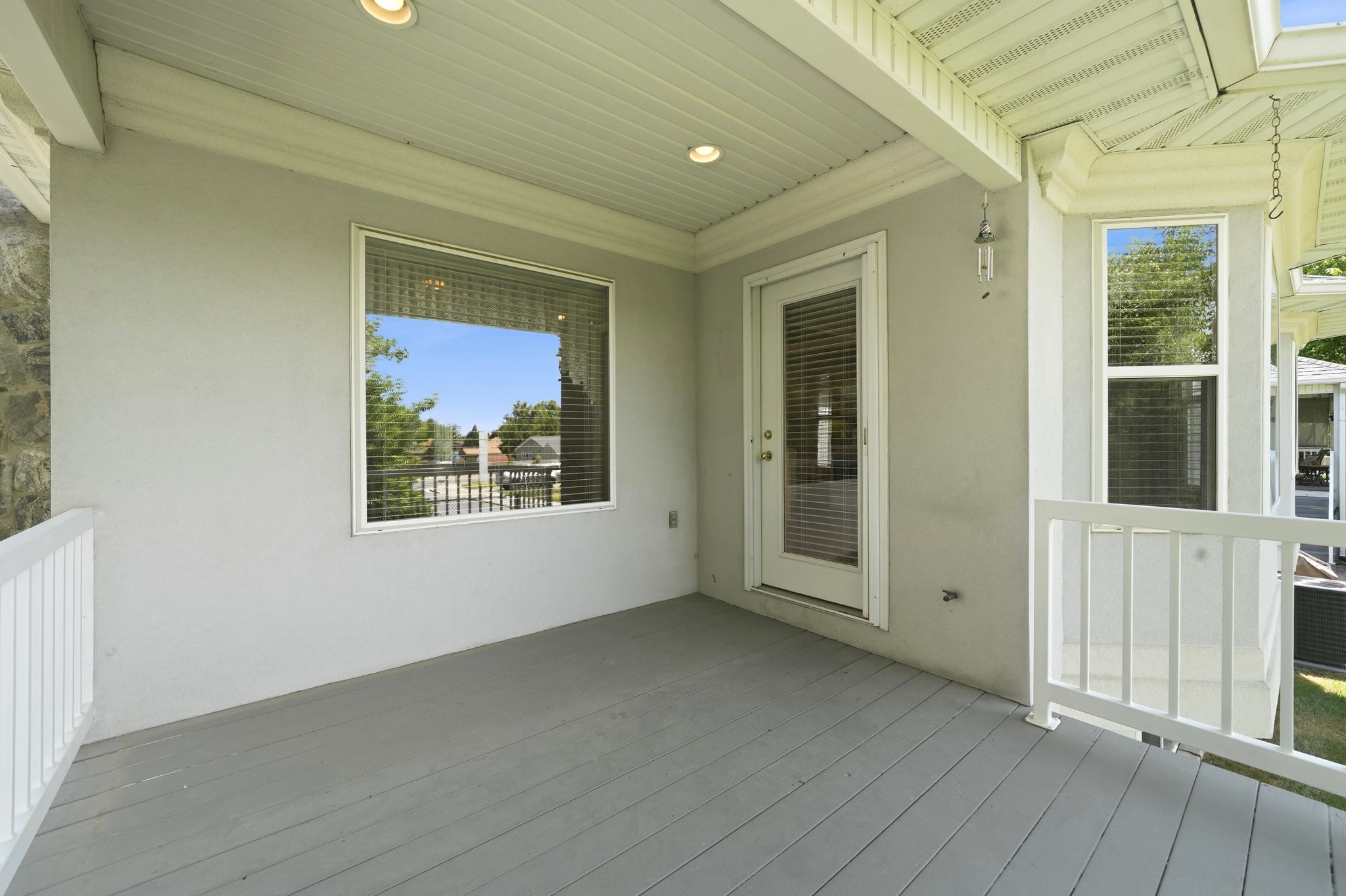 Covered outdoor deck with painted wood-finish flooring, white railing, and recessed lighting