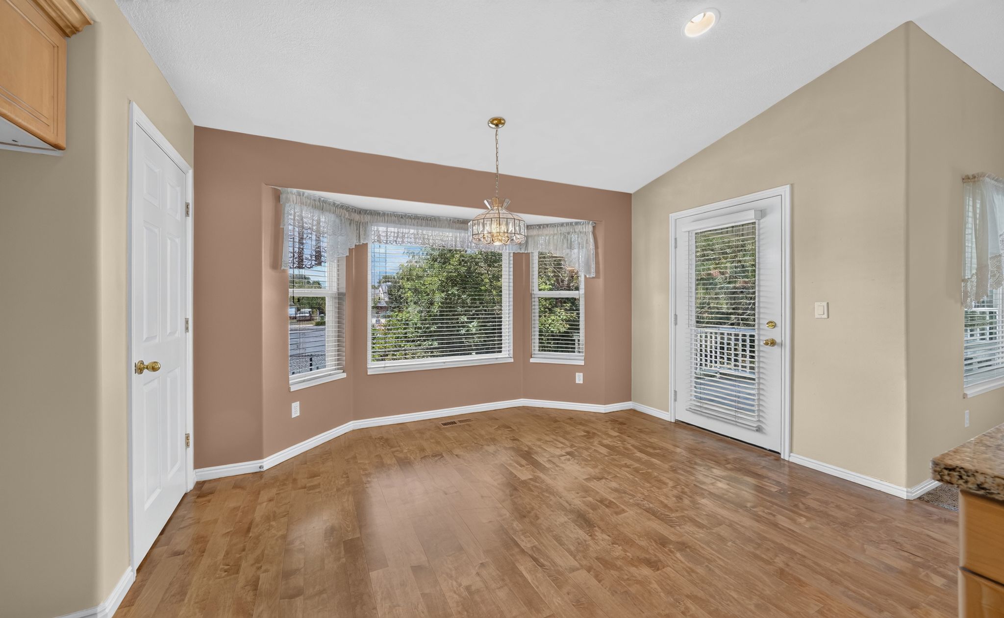 Dining area featuring wood-finish flooring, a bay window with blinds, and a vaulted ceiling