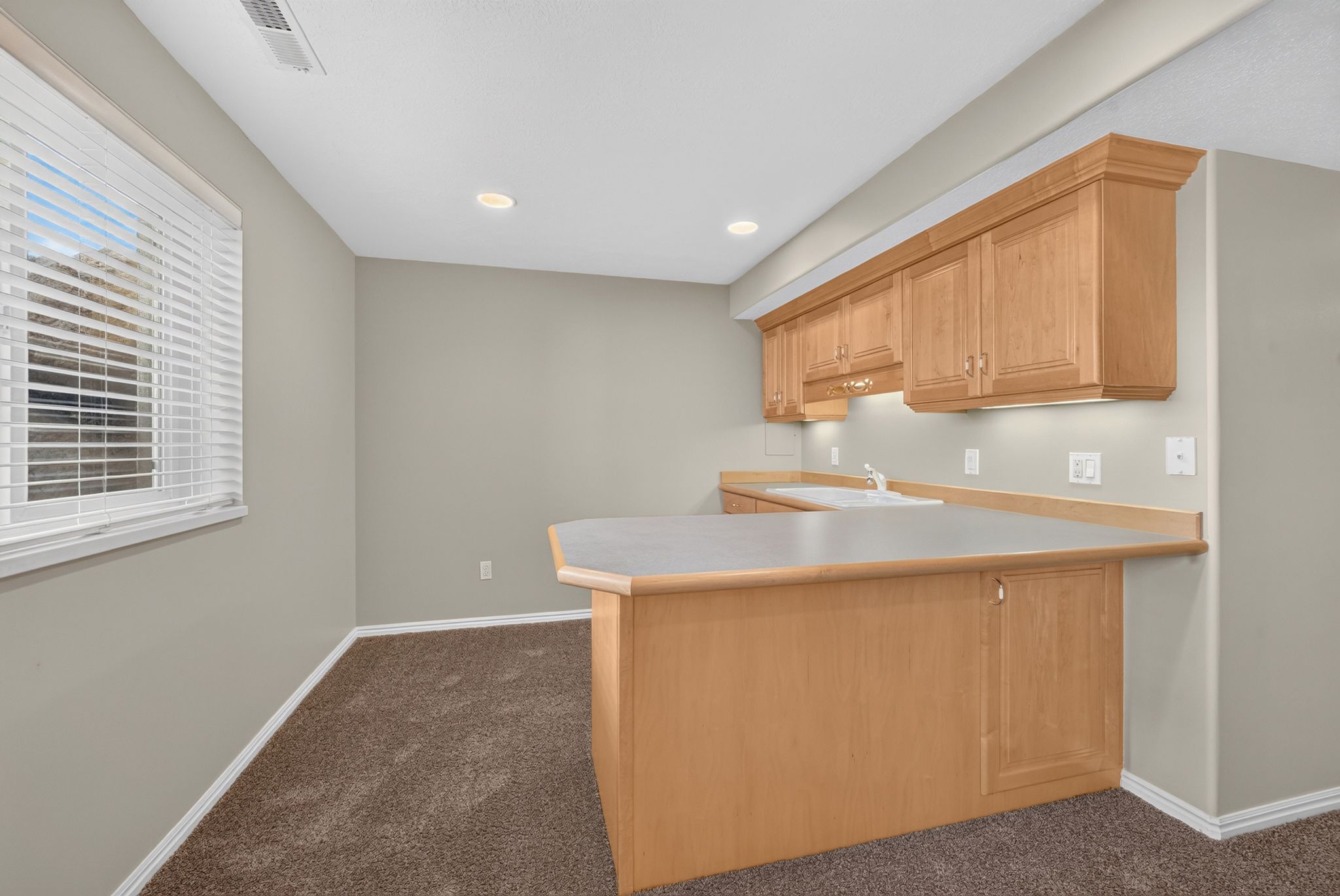 Kitchenette featuring light wood cabinetry, a built-in sink, and a light-toned countertop
